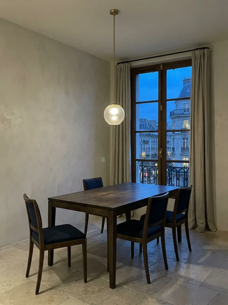 Matte black repeated across pendant, hardware, and chair legs in a Berlin industrial loft dining room with bare brick walls.