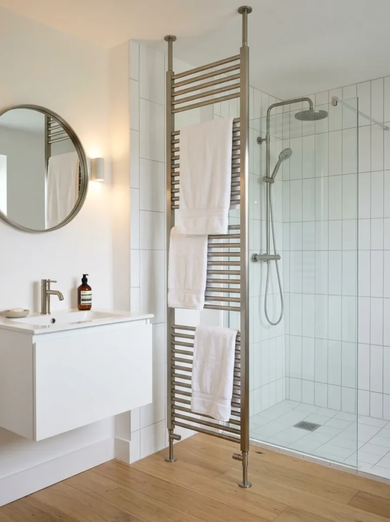 Small bathroom with a tall slimline floor-to-ceiling towel radiator in brushed nickel used as a partial room divider between the shower zone and vanity