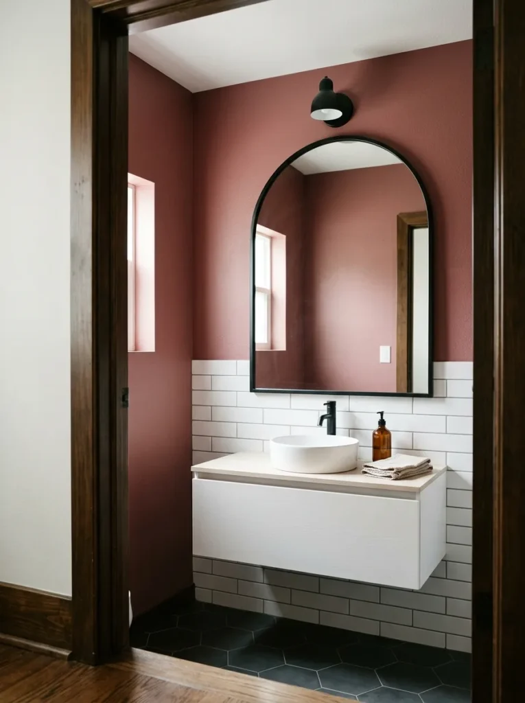 Large arch-top mirror in matte black above a white floating vanity on a deep dusty rose powder room wall
