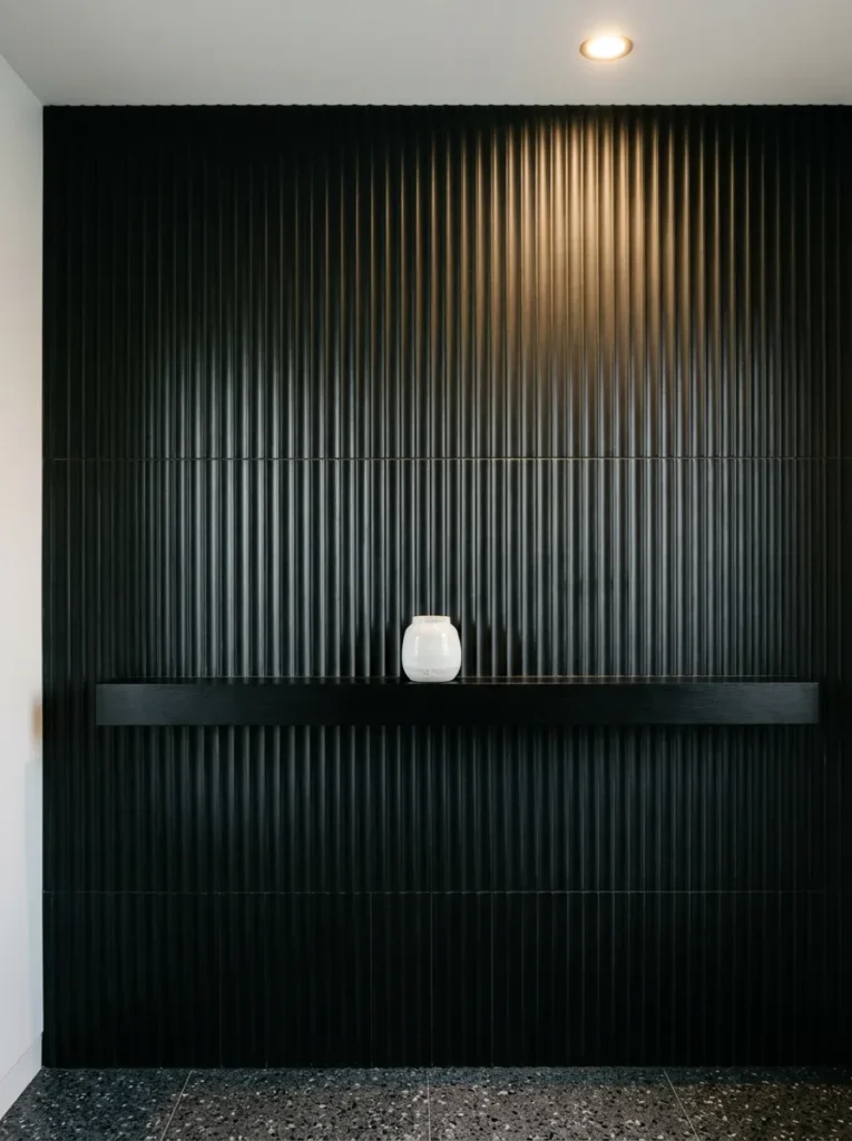 Floor-to-ceiling vertical matte black fluted tile bathroom wall with shadow lines running between channels under recessed downlight