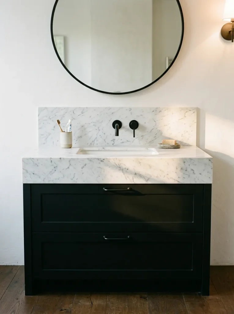 Matte black bathroom vanity with white Carrara marble counter, undermount basin, and slimline black wall tap, shadow line visible under stone overhang