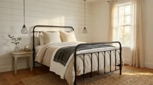 Farmhouse bedroom with matte black iron bed, shiplap accent wall, cage pendant lights, and layered linen bedding on wide plank floors